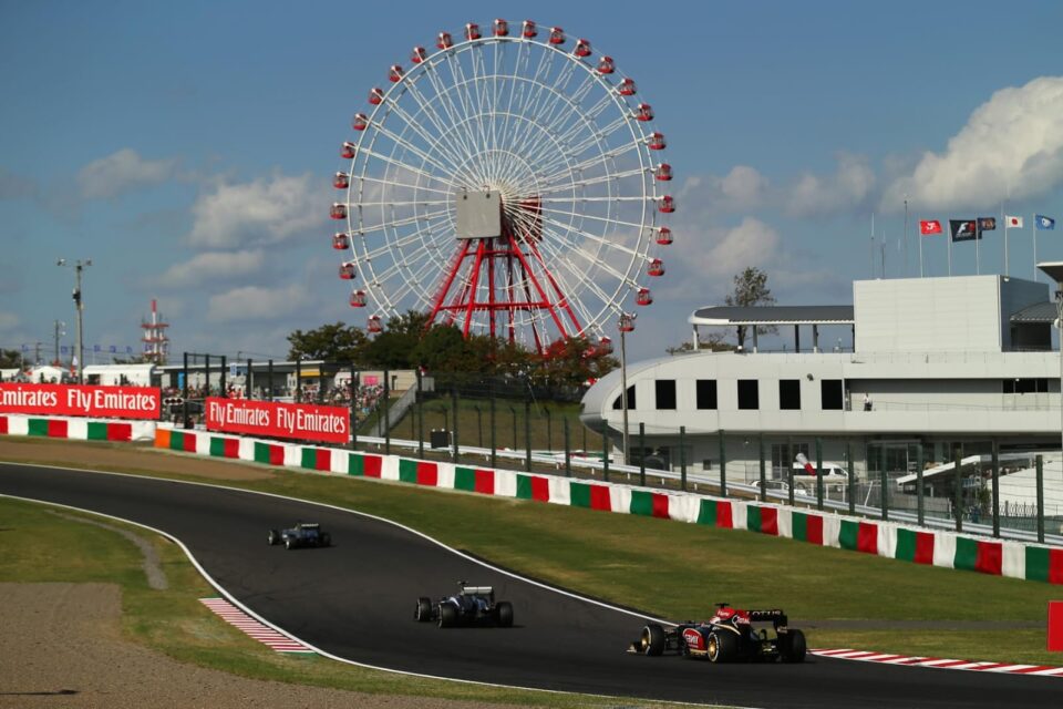 foto mostra trecho do circuito de Suzuka, com três carros automobilísticos na pista. Ao fundo, grande roda gigante completa cenário.